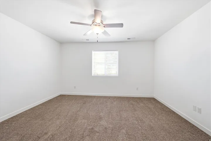 Room featuring neutral carpeting, white walls, a single window with blinds, and a ceiling fan with integrated lighting