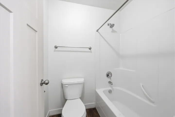 Full bathroom featuring a shower-over-tub combination with a white surround, toilet, and wood-finish flooring