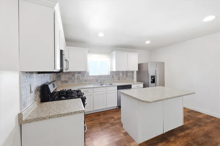 Kitchen featuring white cabinetry, light-toned countertops, a patterned tile backsplash, wood-finish flooring, and recessed lighting
