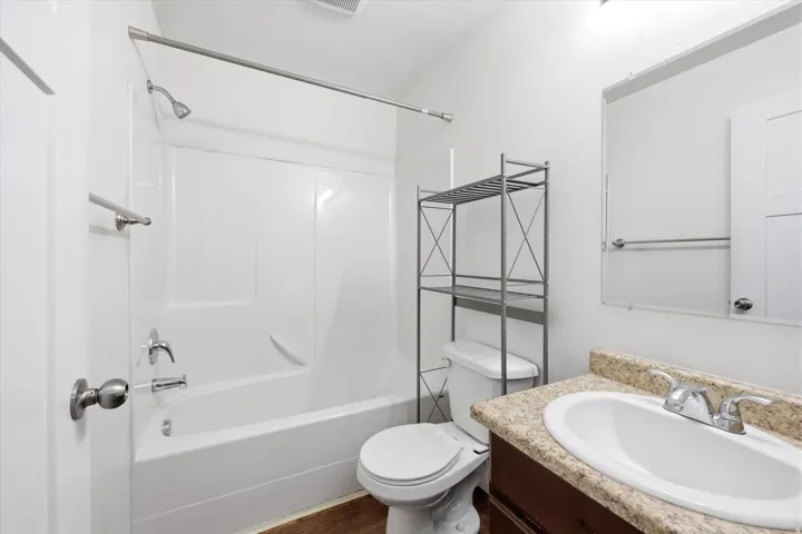 White bathtub with integrated shower, chrome fixtures, dark wood-finish vanity with light speckled countertop, and a white oval sink