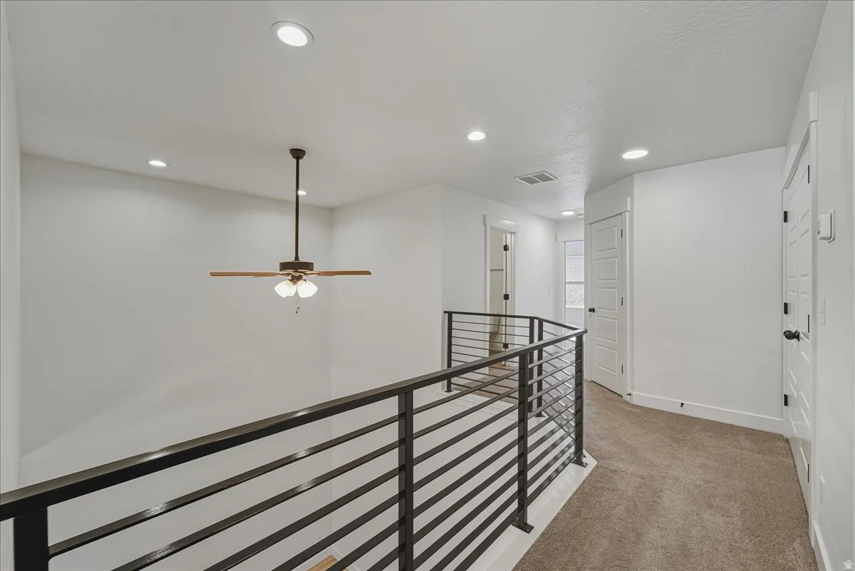 Hall with an upstairs landing, light colored carpet, and recessed lighting
