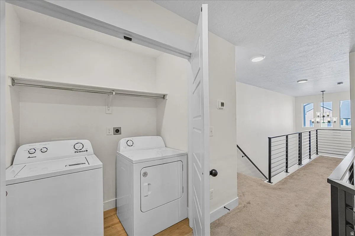 Laundry area featuring a textured ceiling, suspended lighting, washing machine and clothes dryer, and light carpet