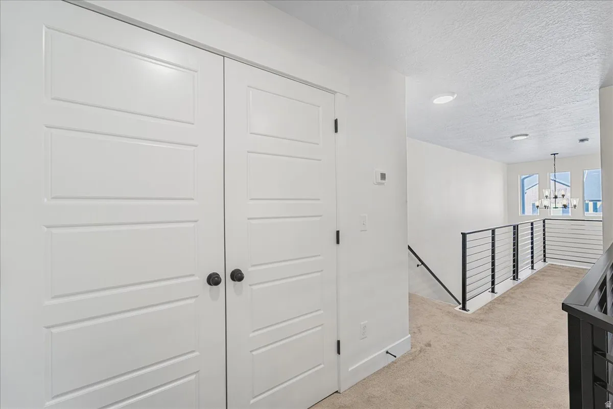 Hallway with an upstairs landing, light colored carpet, a textured ceiling, and a chandelier