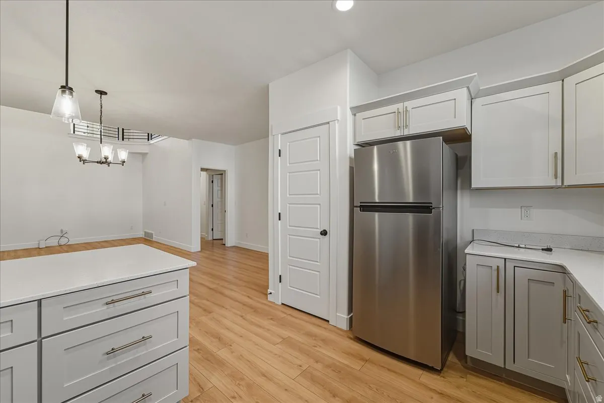 Kitchen with freestanding refrigerator, light wood finished floors, gray cabinets, white cabinets, and suspended lighting