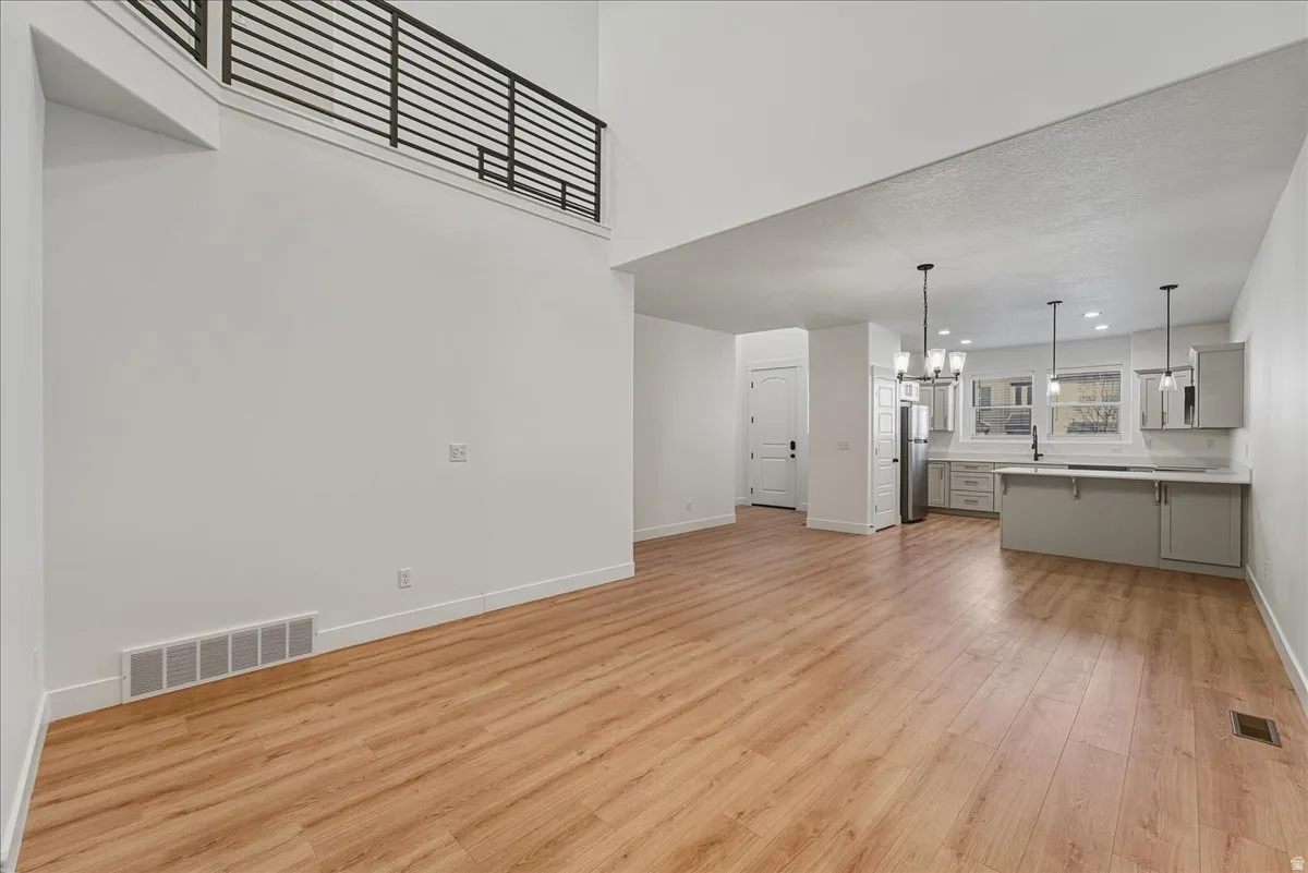 Unfurnished living room with suspended lighting, light wood-style floors, and a high textured ceiling