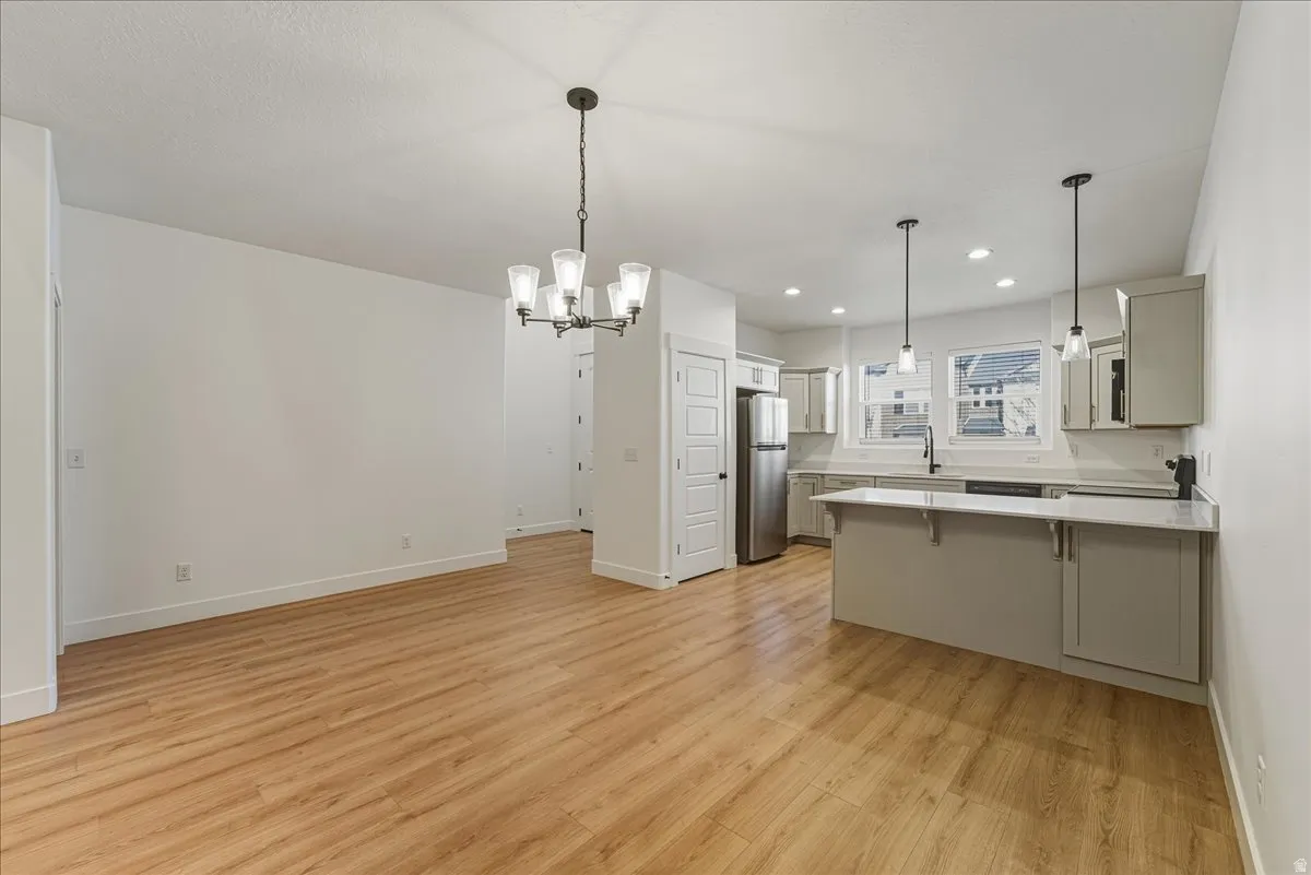 Kitchen with a peninsula, a kitchen breakfast bar, suspended lighting, freestanding refrigerator, and light wood-style floors
