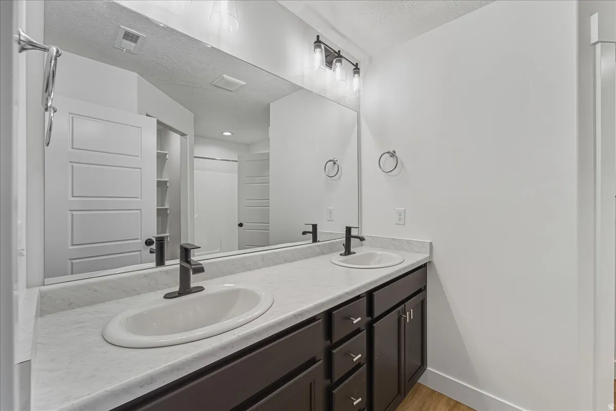 Bathroom with double vanity, a textured ceiling, and light wood-type flooring