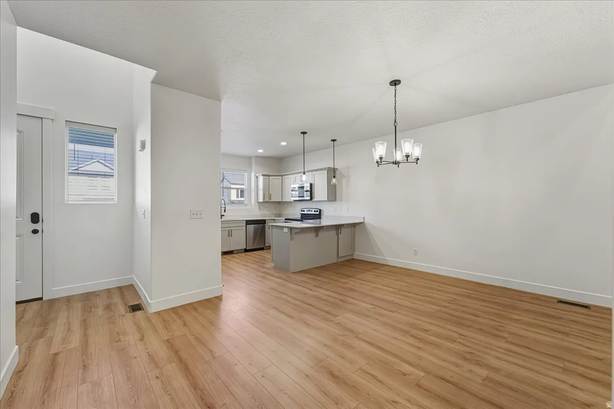 Kitchen with light countertops, a peninsula, hanging lights, light wood-style floors, and stainless steel appliances