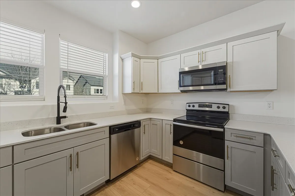 Kitchen with stainless steel appliances, light wood-style flooring, light stone countertops, dual tone cabinetry, and recessed lighting