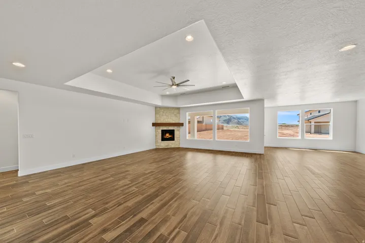 Unfurnished living room featuring a raised ceiling, a stone fireplace, wood tiled floors, recessed lighting, and ceiling fan