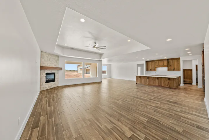 Unfurnished living room with a fireplace, wood finish floors, a ceiling fan, a tray ceiling, and recessed lighting