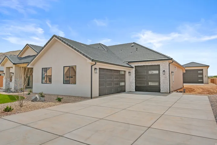 View of front of property with concrete driveway, a tile roof, an attached garage, stucco siding, and stone siding