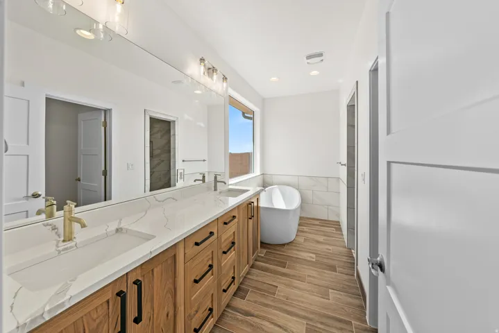 Full bathroom with tile walls, double vanity, a soaking tub, wood tiled floors, and wainscoting