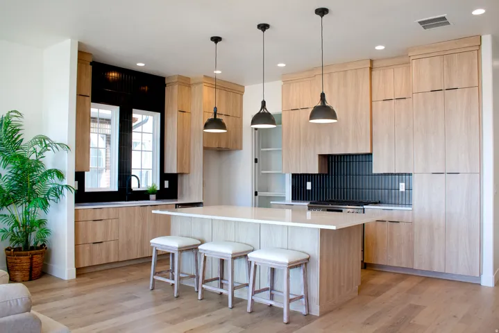 Kitchen with light wood finish cabinetry, a breakfast bar, modern cabinets, pendant lighting, and light stone counters