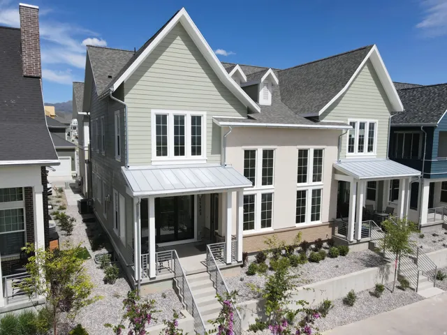 Modern multi-story residence featuring light green siding, white trim, multiple gables, a covered front porch with metal railings, and a stone-lined front landscaping