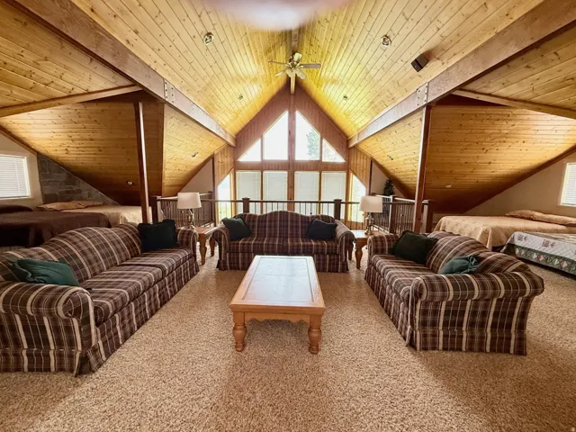 Living room featuring a wooden ceiling with exposed beams, carpet flooring, and ceiling fan