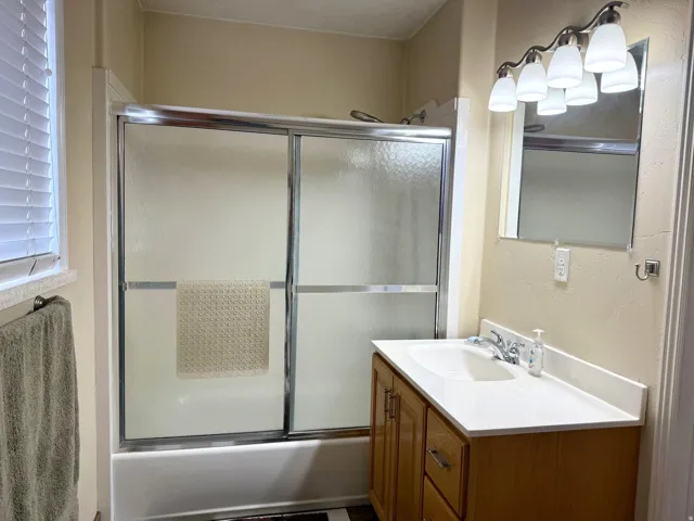 Bathroom with vanity, bath / shower combo with glass door, and a textured wall