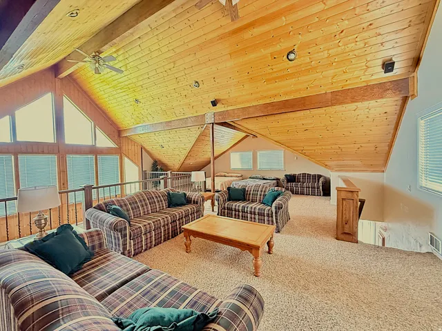 Living room featuring carpet floors, a high wooden beamed ceiling, and a ceiling fan