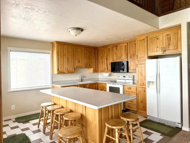 Kitchen with dark floors, white appliances, light countertops, a center island, and a breakfast bar