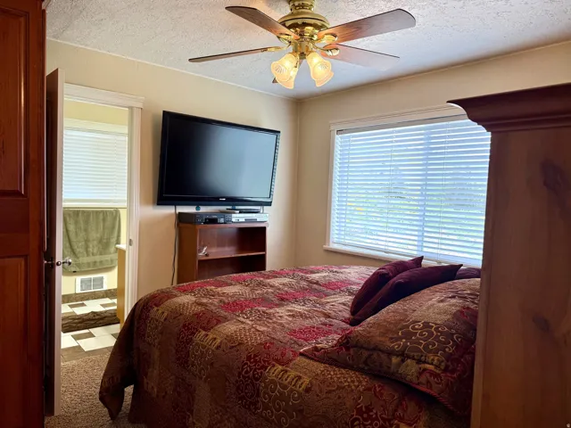 Bedroom featuring ceiling fan, a textured ceiling, connected bathroom, and carpet floors