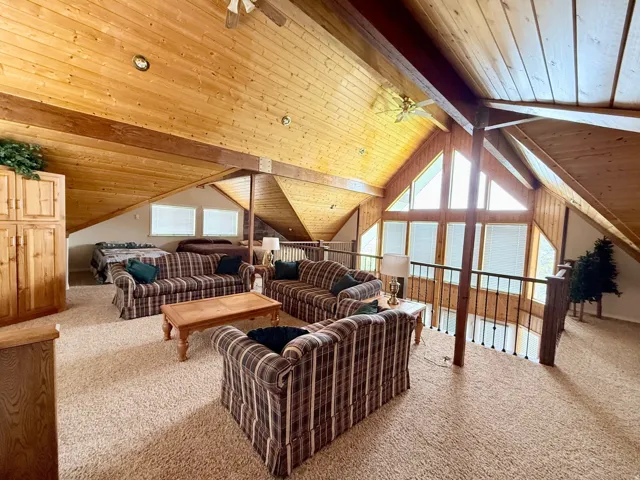 Living area featuring carpet flooring, a ceiling fan, and a wood ceiling with exposed beams