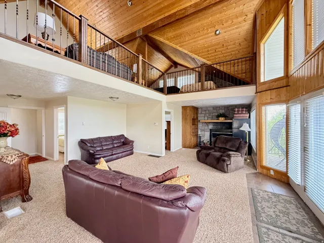 Living area featuring a stone fireplace, a vaulted wooden ceiling, and light colored carpet