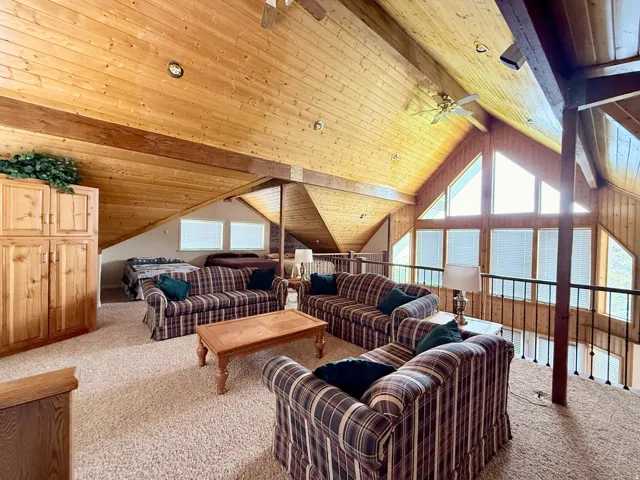 Carpeted living area featuring a wooden ceiling with exposed beams and a ceiling fan