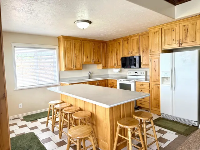 Kitchen featuring white appliances, light flooring, light countertops, a center island, and a kitchen breakfast bar