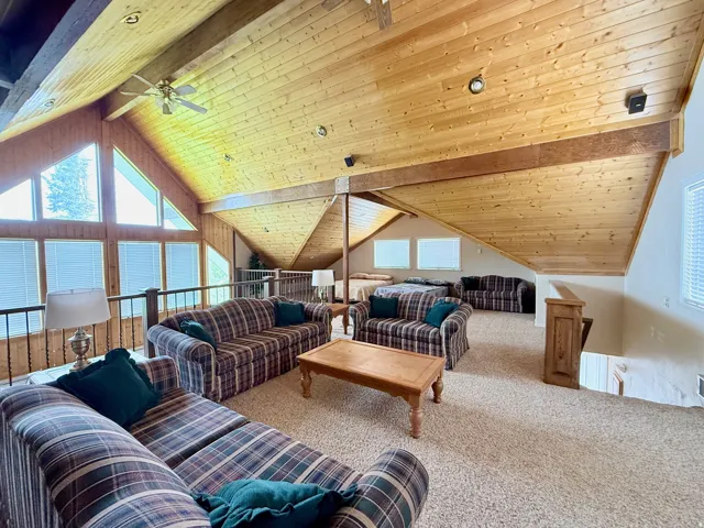 Living area with carpet, a wooden ceiling with exposed beams, and ceiling fan
