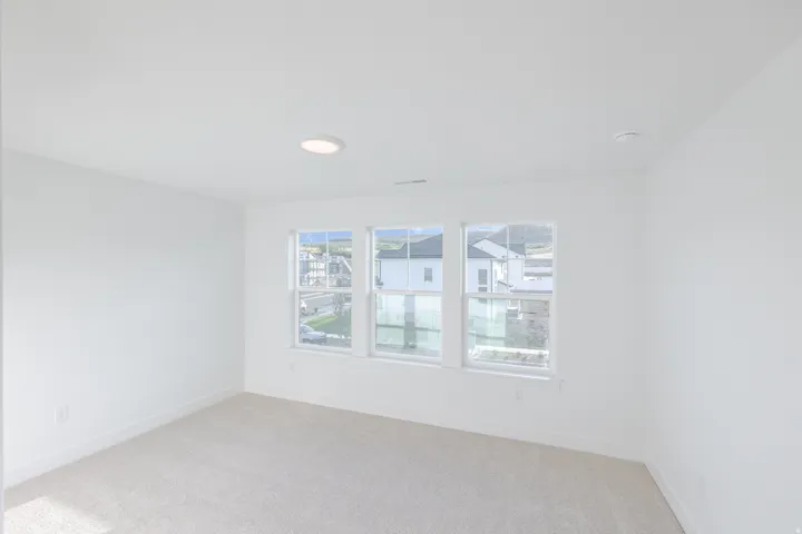 Bright interior space featuring three large windows, neutral carpeting, white baseboards, and a flush-mount ceiling light fixture