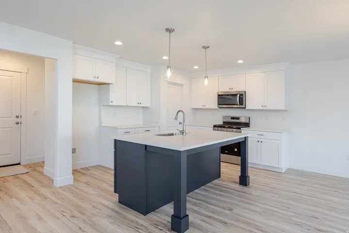 Modern kitchen featuring a central island with a sink, white cabinetry, stainless steel appliances, light wood-finish flooring, and recessed lighting