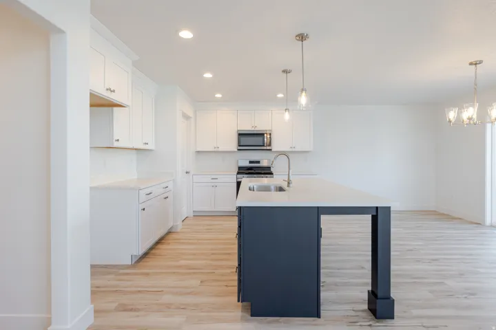 Spacious kitchen featuring white shaker-style cabinetry, a dark blue island with integrated sink, stainless steel appliances, recessed lighting, and wood-finish flooring