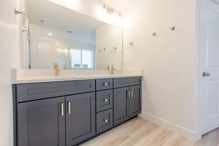 Dual vanity with dark shaker-style cabinetry, a light-toned countertop, and gold-finish fixtures
