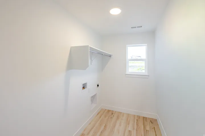 Laundry room featuring wood-finish flooring, a single window, a built-in recessed light, and a dedicated utility area with wall-mounted shelving and a clothing rod