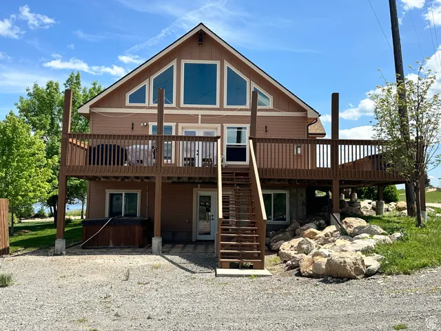 Back of house featuring a wooden deck, a hot tub, board and batten siding, and a patio