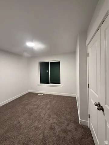 Unfurnished room featuring baseboards and dark colored carpet