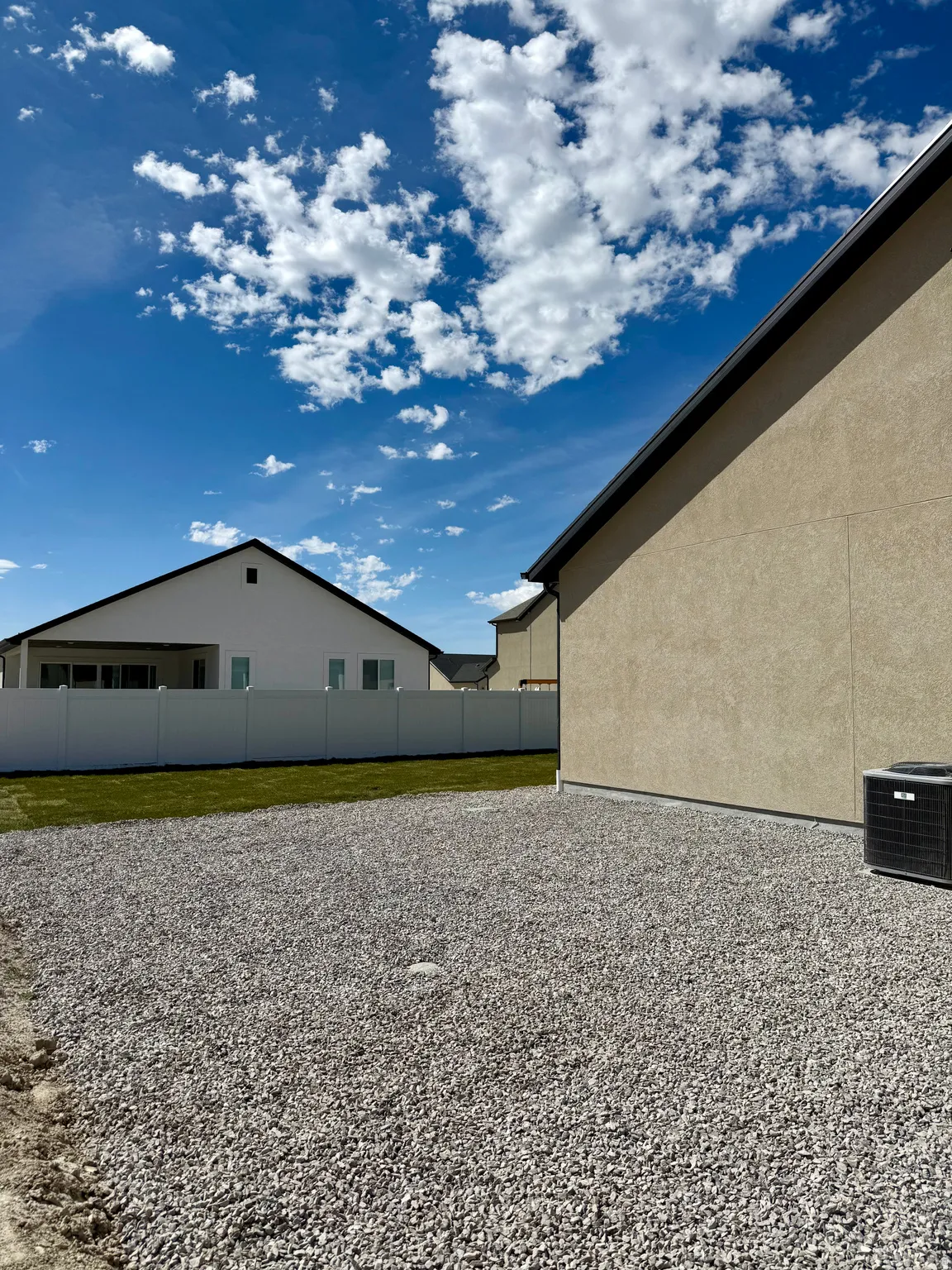 Expansive gravel and grass outdoor space with a white privacy fence