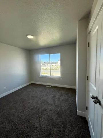 Recessed ceiling light, neutral wall paint, dark carpet flooring, and a white-trimmed window