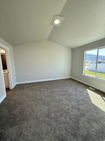 Spacious room with sloped ceiling, recessed lighting, expansive window, and plush carpeting
