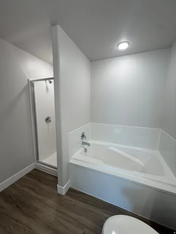 White bathtub with chrome fixtures, enclosed shower with clear glass, recessed ceiling lighting, and Lvp