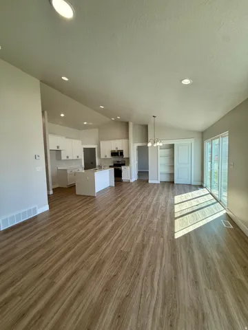 Open-concept living space featuring Lvp, vaulted ceilings with recessed lighting, a kitchen island, white cabinetry, and sliding glass doors
