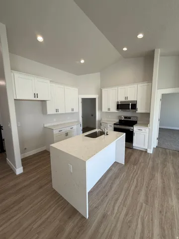 Vaulted ceilings, recessed lighting, white cabinetry with dark hardware, a kitchen island with an integrated sink, and lvp