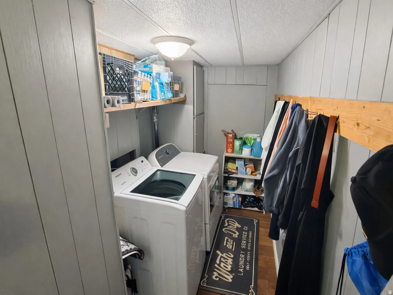 Laundry room with wood walls, washer and dryer, dark wood-type flooring, and a textured ceiling