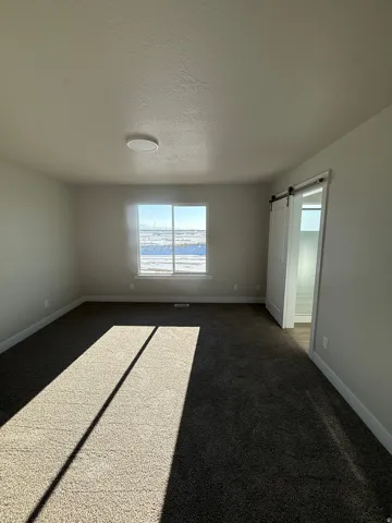 Unfurnished room with dark colored carpet, a barn door, and a textured ceiling