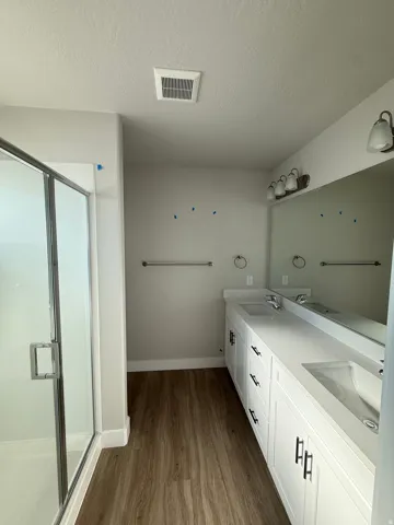 Full bathroom featuring double vanity, a shower stall, light wood finished floors, and a textured ceiling