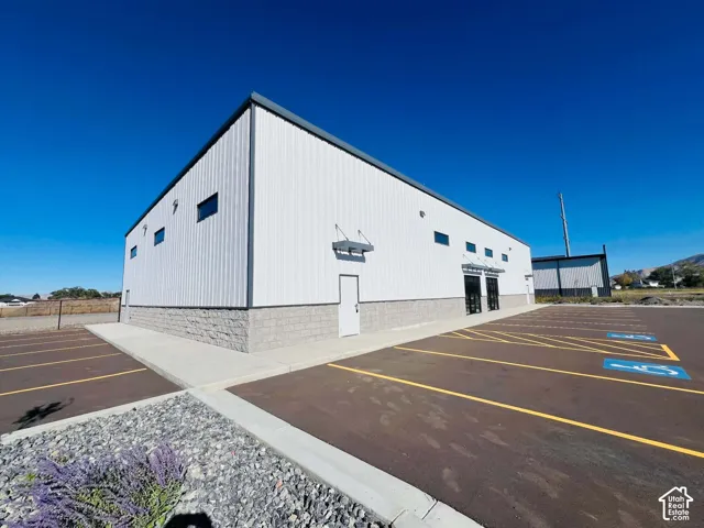 Industrial structure featuring a ribbed metal exterior, masonry base, paved parking lot with marked stalls, and high-set windows