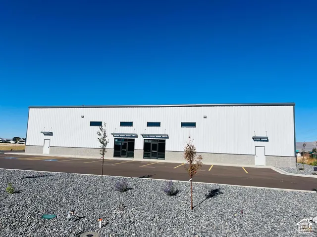 Commercial structure featuring a metal exterior, stone masonry base, multiple glass-panel entry doors, transom windows, and an asphalt parking area
