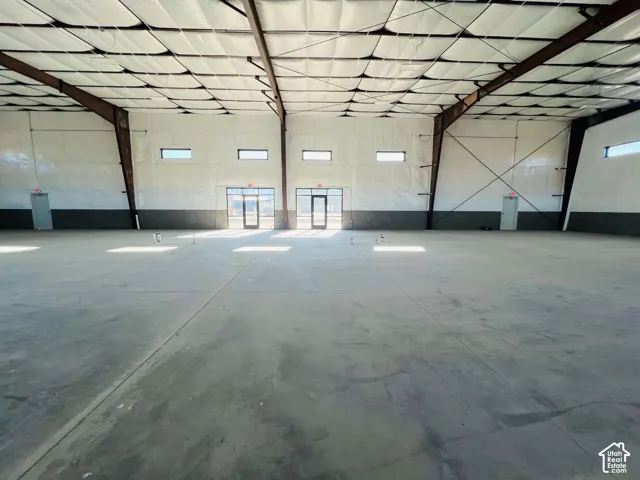 Open-span industrial interior featuring high ceilings with exposed steel beams, insulated wall paneling, concrete flooring, and multiple glass-entry doors