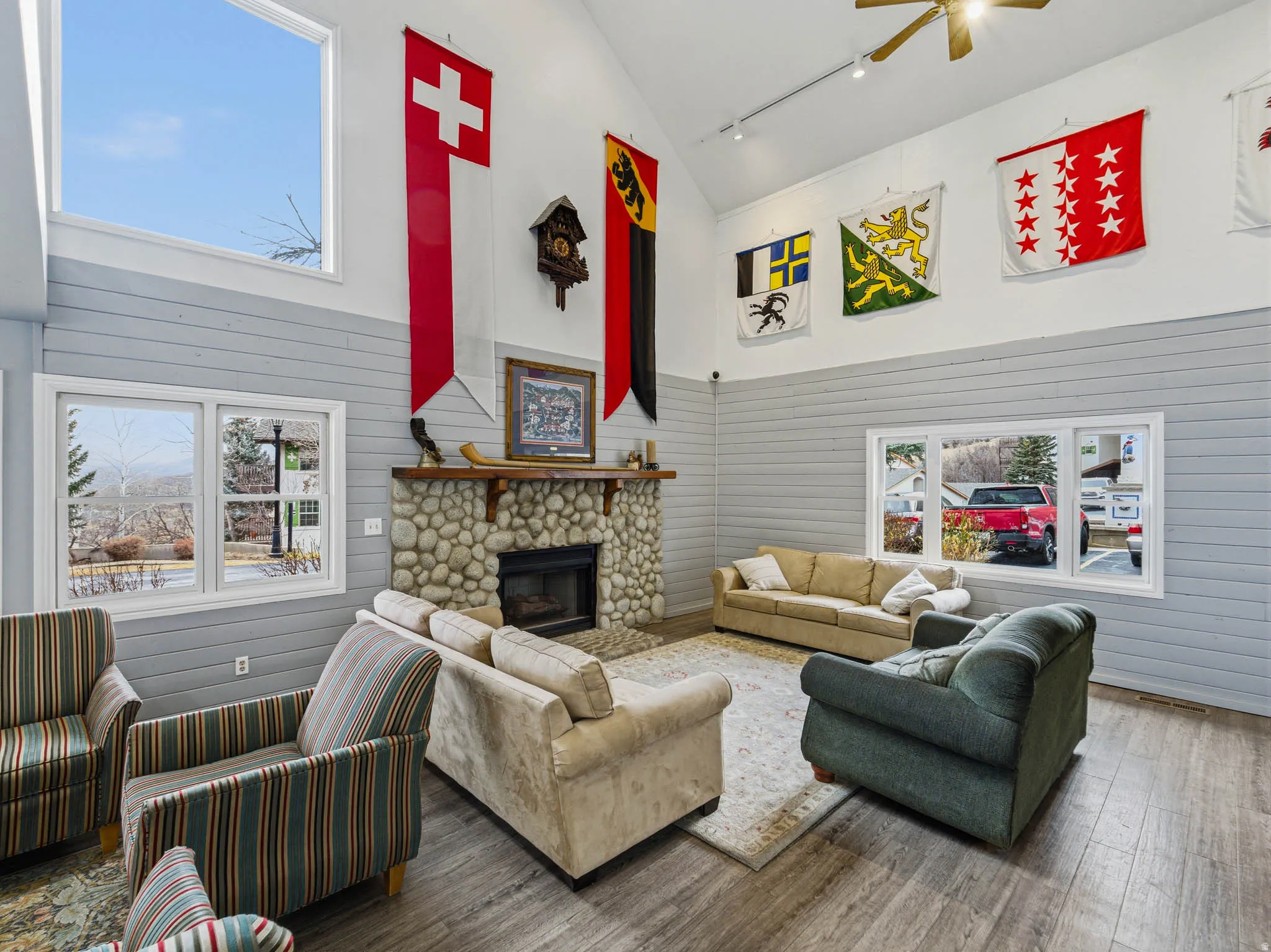 Living area with healthy amount of natural light, rail lighting, vaulted ceiling, a ceiling fan, and a stone fireplace