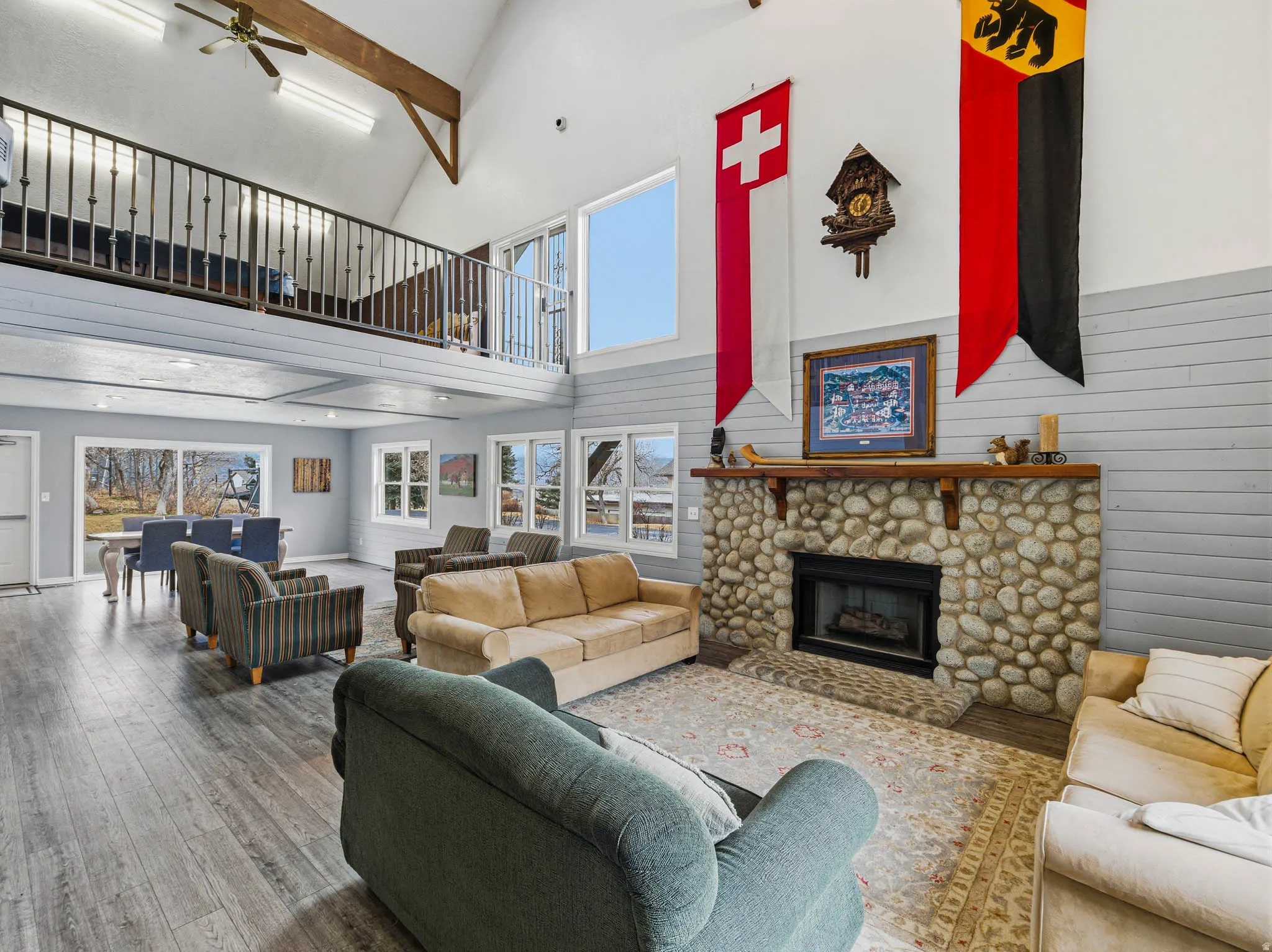 Living area featuring a ceiling fan, hardwood / wood-style flooring, a stone fireplace, wood walls, and vaulted ceiling